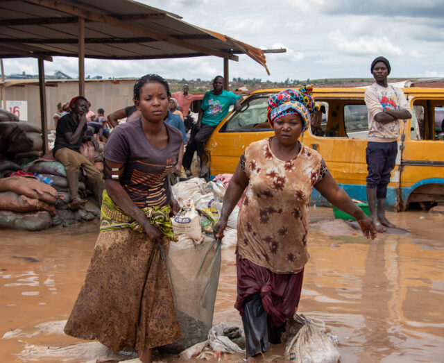 two ladies carrying a large bag of items through flooded waters, wading up to their calves