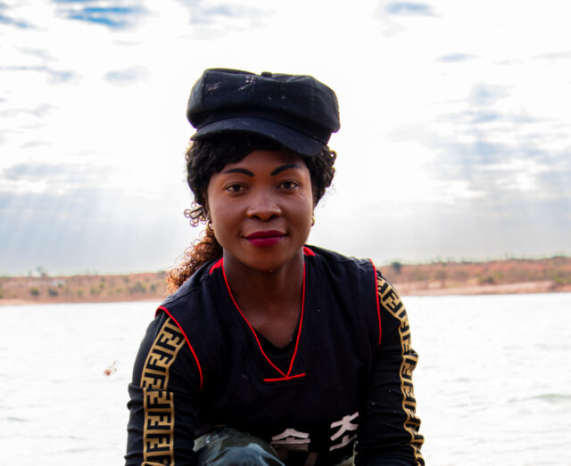 a black female crouched down in ankle-deep water displaying the rocks she is cleaning in a brown sack