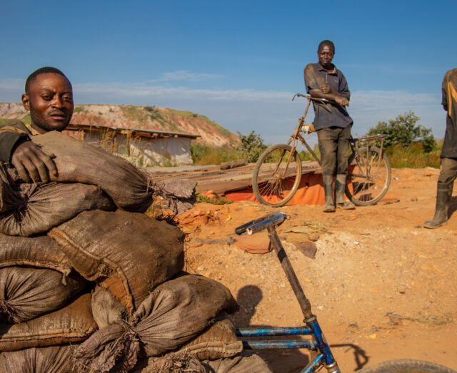 three males standing around bags of mineral ore with two bicycles