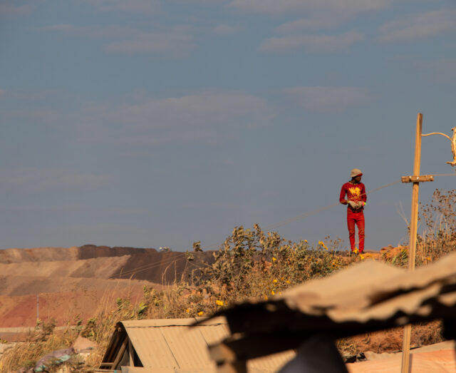 a miner dressed in red standing with the sky as a backdrop, staring to the left